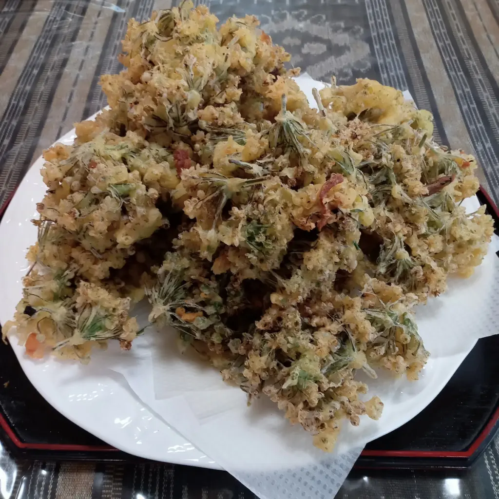 摘み取ったニラの花に衣をつけて油で揚げ、天ぷらにしたところ。白い皿に山盛り。