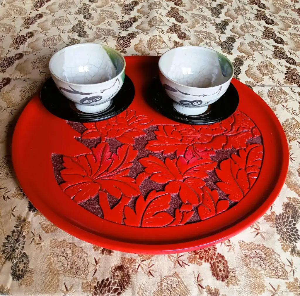 村上木彫堆朱、牡丹柄の丸盆に織部焼の湯飲み茶碗を二客載せて運ぶところ。