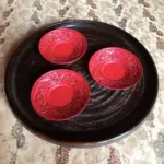 村上木彫堆朱の唐草牡丹柄の茶托３枚が黒い木彫りの丸盆に載せられている。