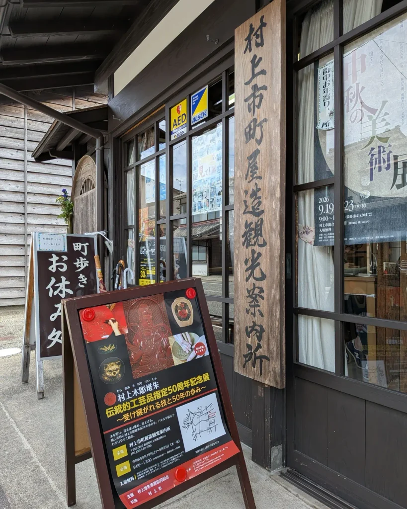 村上市町屋造観光案内所の入口に置かれた村上木彫堆朱 伝統的工芸品指定50周年記念展の案内看板
