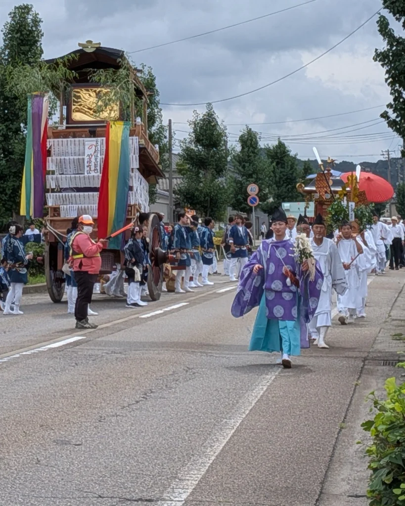 瀬波大祭の屋台の脇を進む神輿渡御の一行