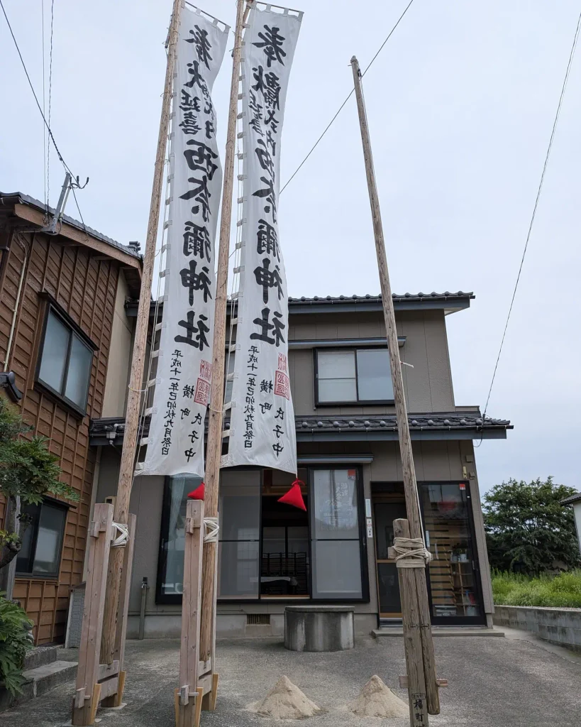 瀬波大祭の瀬波横町のお旅所。川崎家前の井戸と二つの砂盛、幟が見える