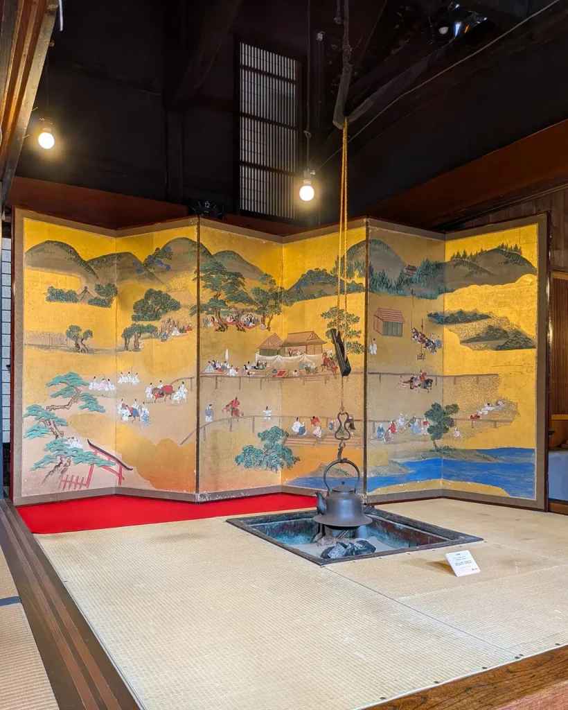 千年鮭きっかわの囲炉裏越しに展示された金地の屏風「上賀茂神社「くらべうま」ご神事絵図」