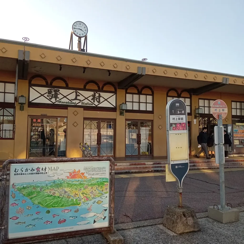 新潟県村上市のJR村上駅。時計のある駅舎と、駅前の観光案内板やバス停